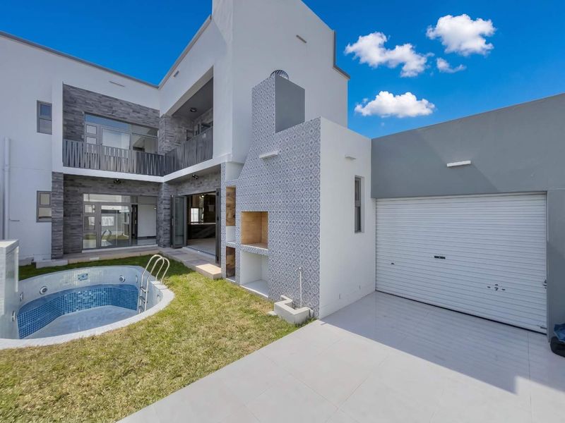Modern rear exterior featuring a swimming pool, built-in braai area, tiled patio, and access to the garage and upper-level balcony.