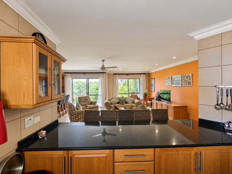Spacious open-plan living area featuring a functional kitchen with granite countertops and oak cabinetry, flowing seamlessly into a bright lounge with balcony access.
