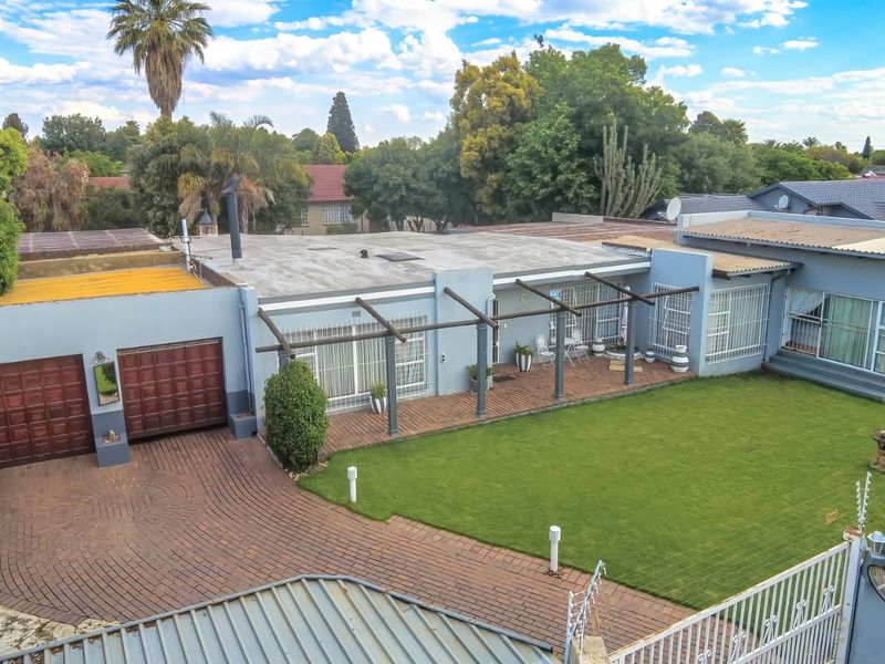 Aerial view of a residential property featuring a paved driveway, double garage, covered patio area with a pergola, and a well-maintained lawn.