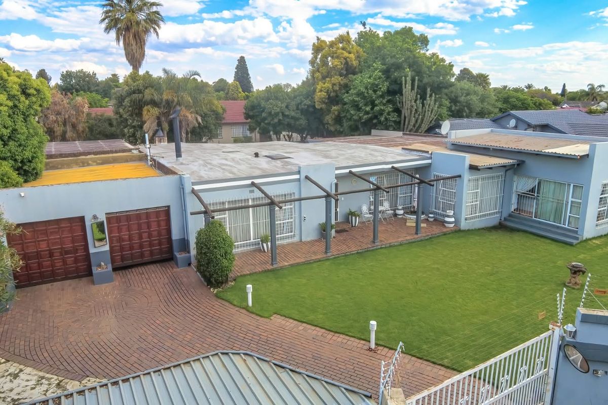 Aerial view of a residential property featuring a paved driveway, double garage, covered patio area with a pergola, and a well-maintained lawn.