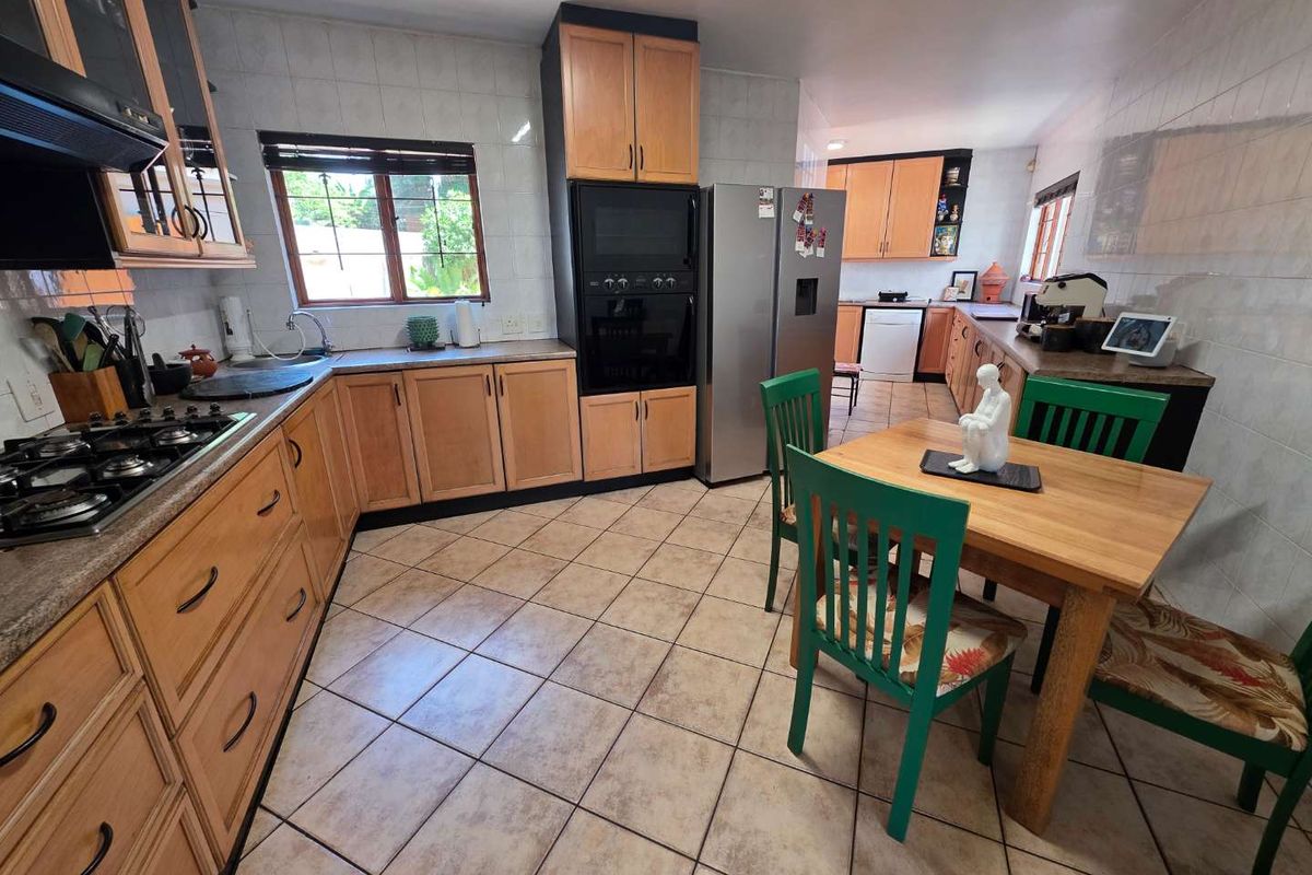 A functional kitchen featuring wooden cabinetry, tiled flooring, built-in oven, and gas hob, offering a practical layout with integrated dining space.