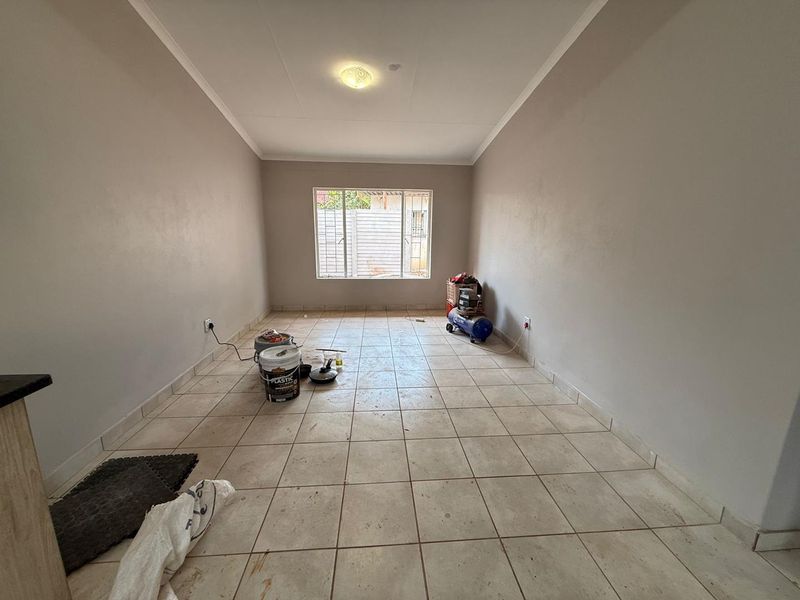 An empty living room featuring tiled flooring, neutral walls, and a window with security bars, offering a blank canvas for interior design.