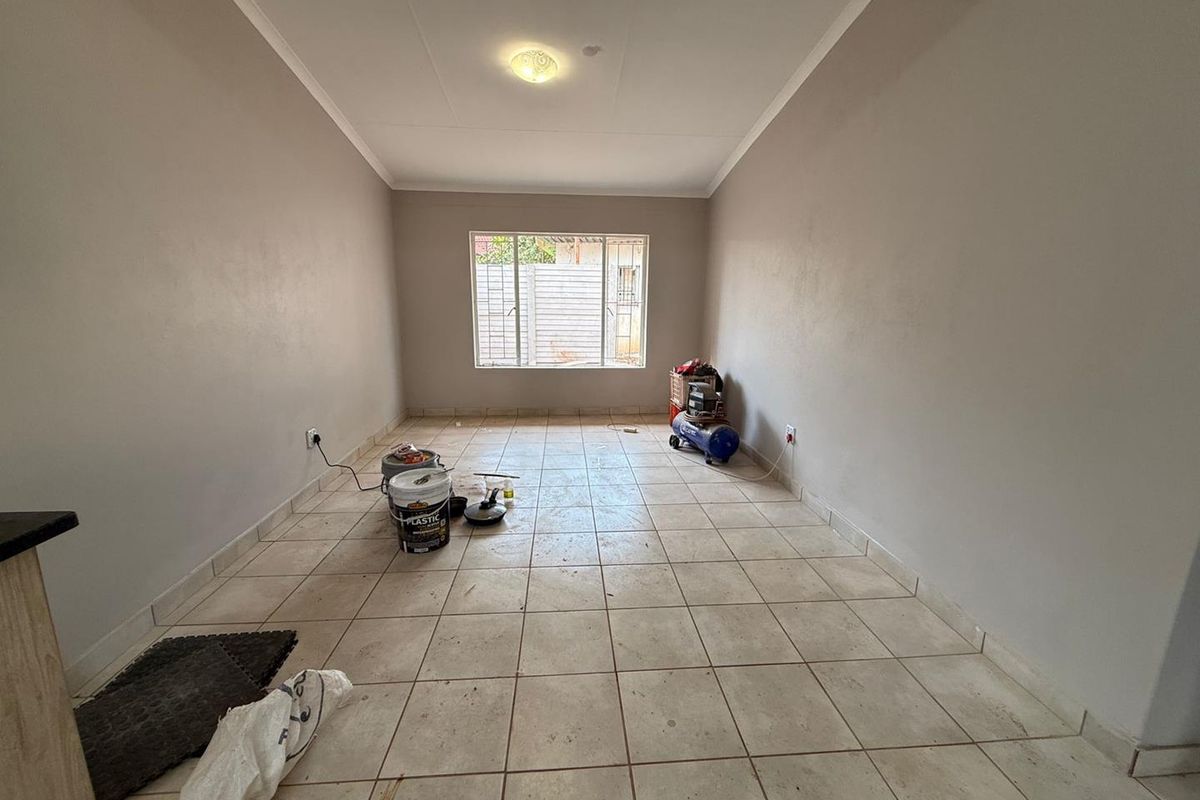 An empty living room featuring tiled flooring, neutral walls, and a window with security bars, offering a blank canvas for interior design.