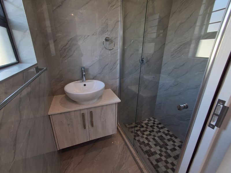 Modern bathroom featuring a vessel sink with vanity cabinet, glass-enclosed shower, and contemporary grey marble-look wall tiles.