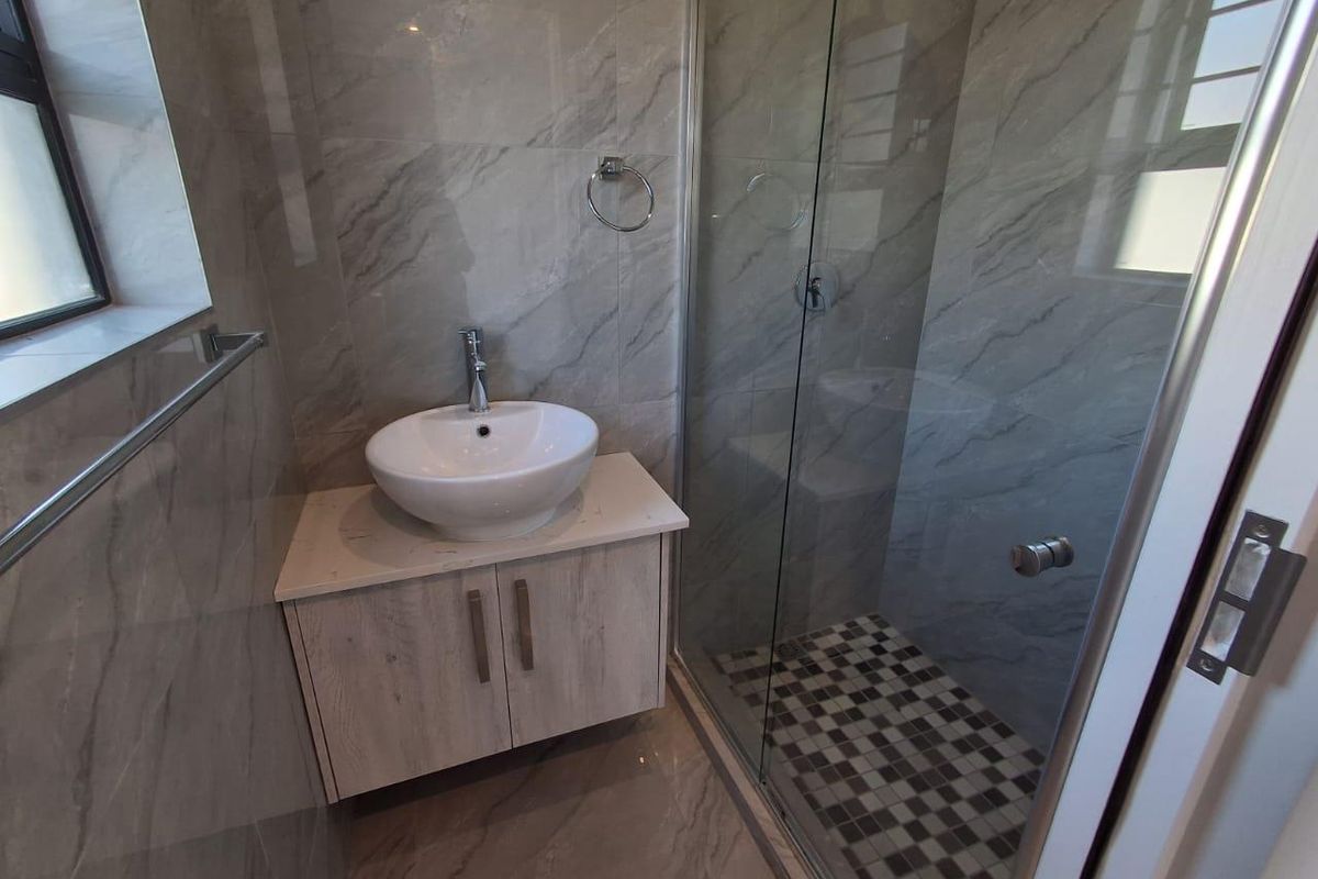 Modern bathroom featuring a vessel sink with vanity cabinet, glass-enclosed shower, and contemporary grey marble-look wall tiles.
