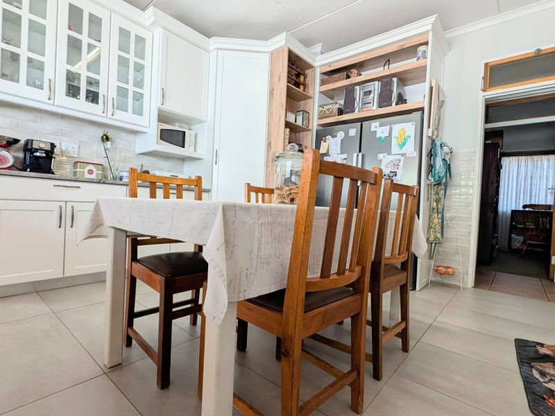 A well-maintained kitchen featuring white cabinetry, stone countertops, a tiled backsplash, and integrated shelving, offering a clean and functional cooking and dining space.