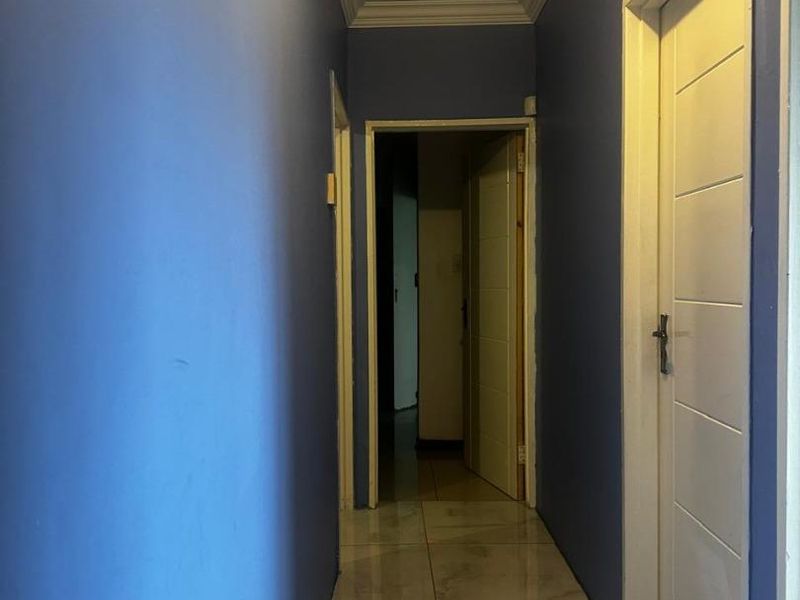 A clean, empty hallway featuring tiled flooring and crown molding, providing access to multiple rooms within the home.