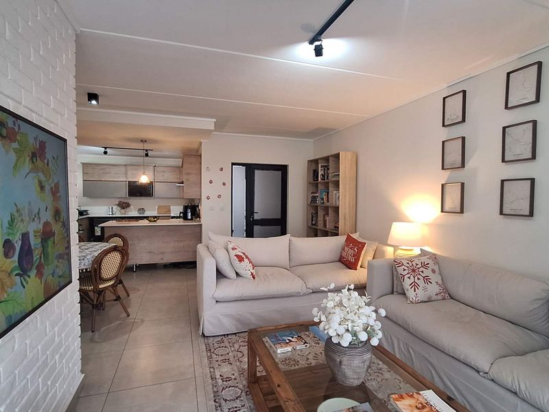 Spacious open-plan living area featuring tiled floors, an exposed brick feature wall, track lighting, and a modern kitchen with a central island.