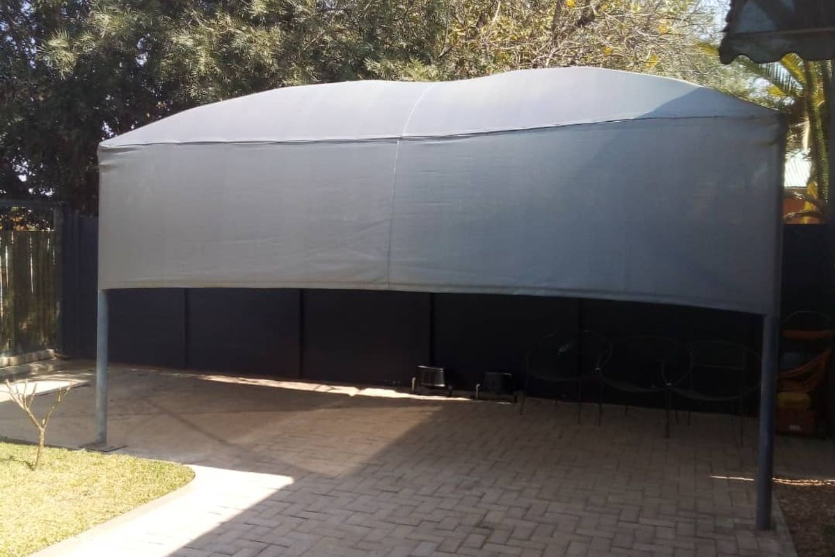 A paved outdoor area featuring a grey shade cloth carport structure, providing covered parking space within a fenced rear yard setting.
