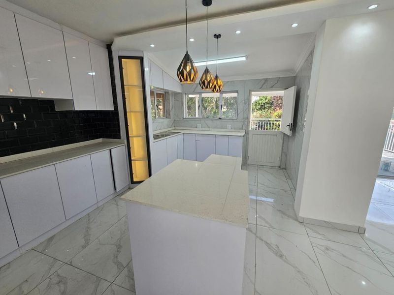Modern, bright kitchen featuring white cabinetry, stone countertops, a central island, and elegant marble-look floor tiles with direct access to the exterior.