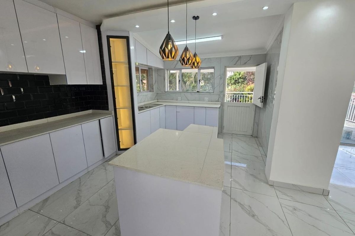 Modern, bright kitchen featuring white cabinetry, stone countertops, a central island, and elegant marble-look floor tiles with direct access to the exterior.