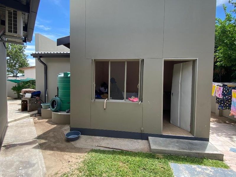 Rear view of the property showing a detached structure, concrete paving, and a water tank in the backyard area.