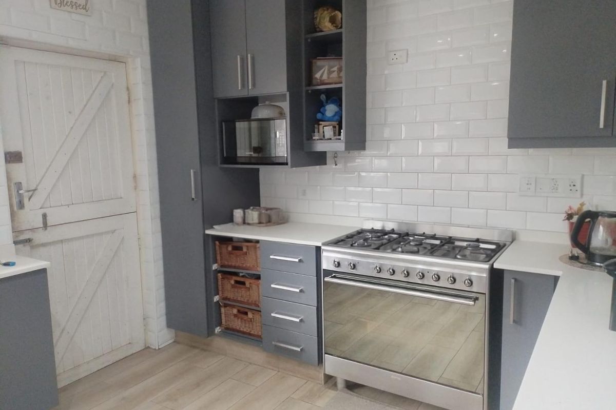 Modern kitchen featuring grey cabinetry, subway tile backsplash, gas stove with oven, and a classic stable door.