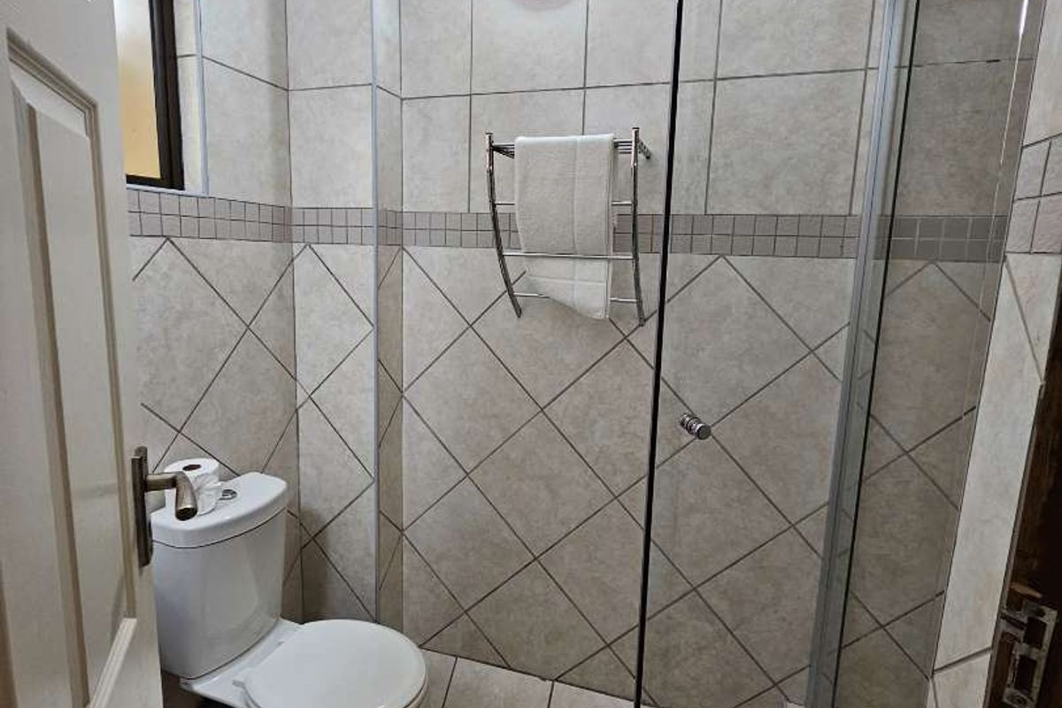 A compact bathroom featuring a glass-enclosed shower, ceramic wall and floor tiling, and a standard toilet.