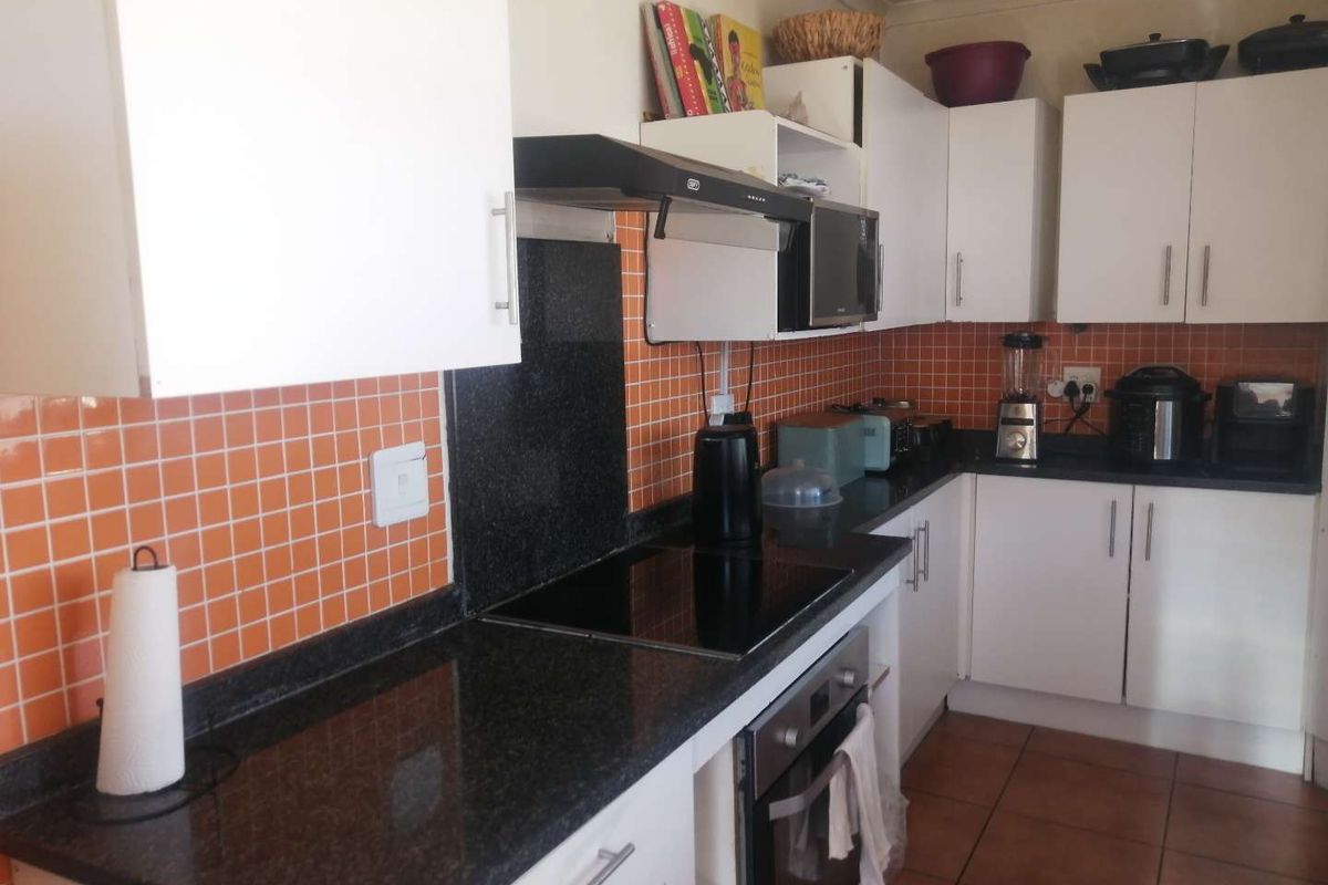 A functional kitchen featuring white cabinetry, dark granite countertops, a built-in oven, and a black extractor fan with orange tiled splashbacks.