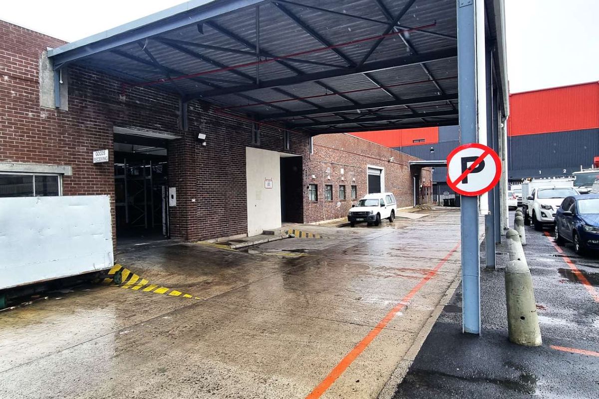 Industrial loading bay area featuring a covered canopy, brick facade, and concrete hardstand, suitable for goods receiving and logistics operations.