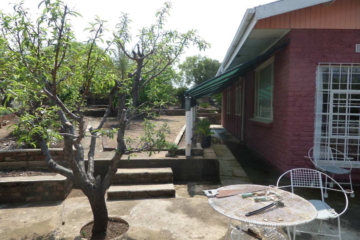 Rear exterior view featuring a concrete patio area, brick retaining walls, and a covered walkway along the side of the house.