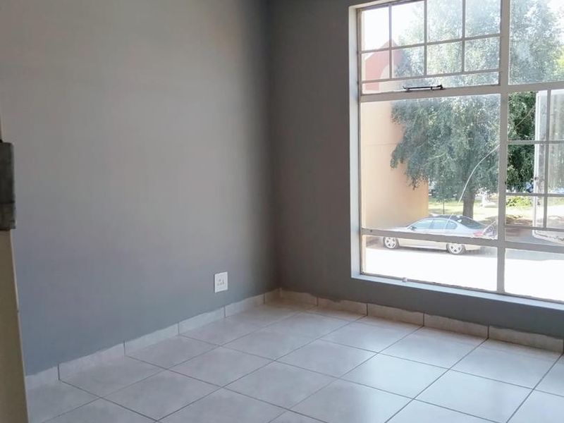 A bright, empty bedroom featuring neutral grey walls, tiled flooring, and a large window providing natural light and street views.