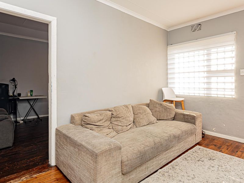 A living room featuring timber flooring, roller blinds, and access to an adjacent room and balcony area.