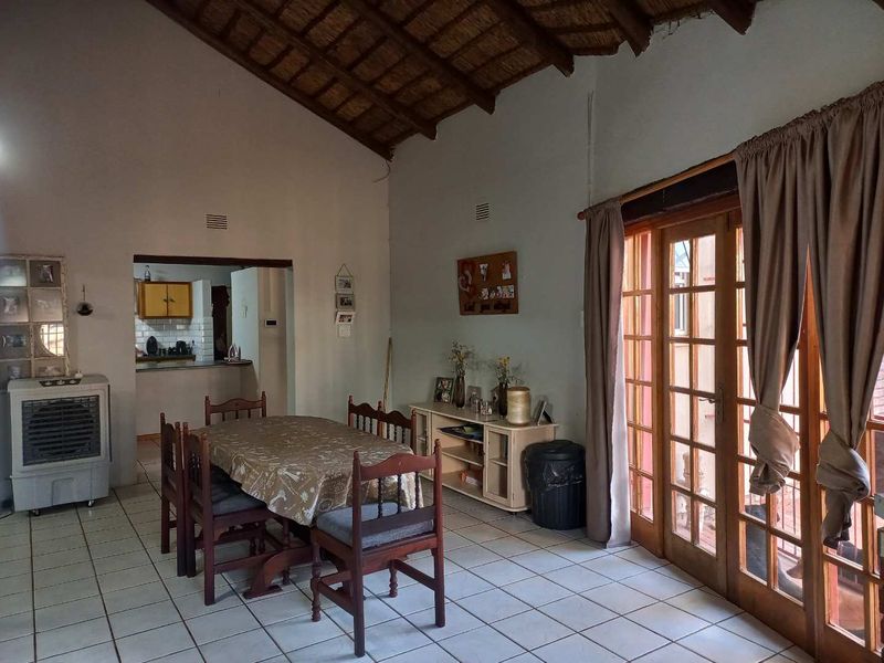 Open-plan dining area featuring exposed thatch vaulted ceilings, ceramic tiled flooring, and timber-framed glass doors providing access to the exterior.
