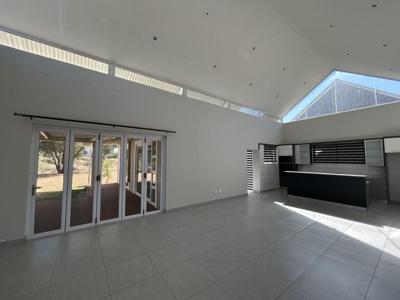 Spacious open-plan living area featuring a vaulted ceiling, clerestory windows, tiled floors, and seamless access to the outdoor patio through bi-fold doors.