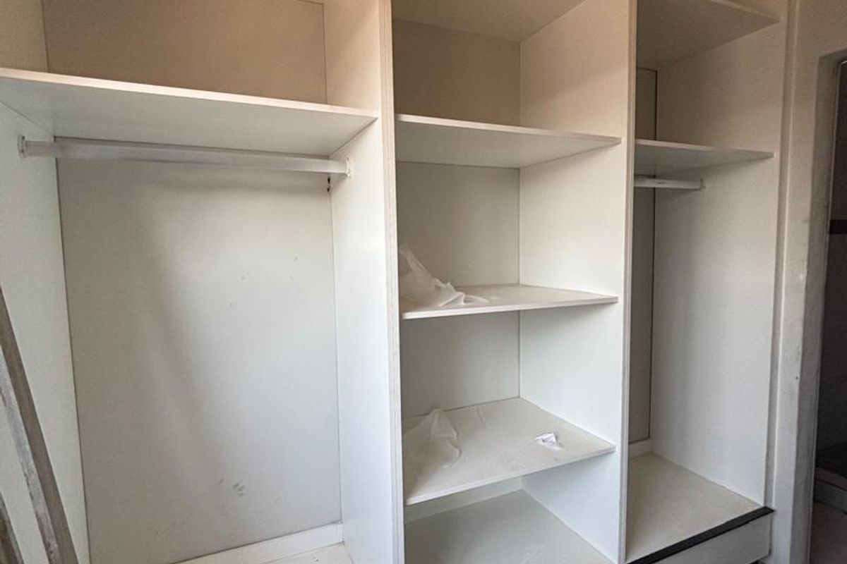A functional built-in wardrobe featuring multiple shelving sections and hanging rails, providing ample storage space within the bedroom.