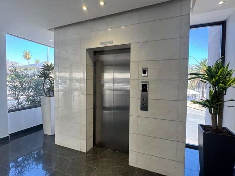 Modern office building lobby featuring a stainless steel elevator, polished stone floor tiles, and elegant stone wall cladding with recessed lighting.