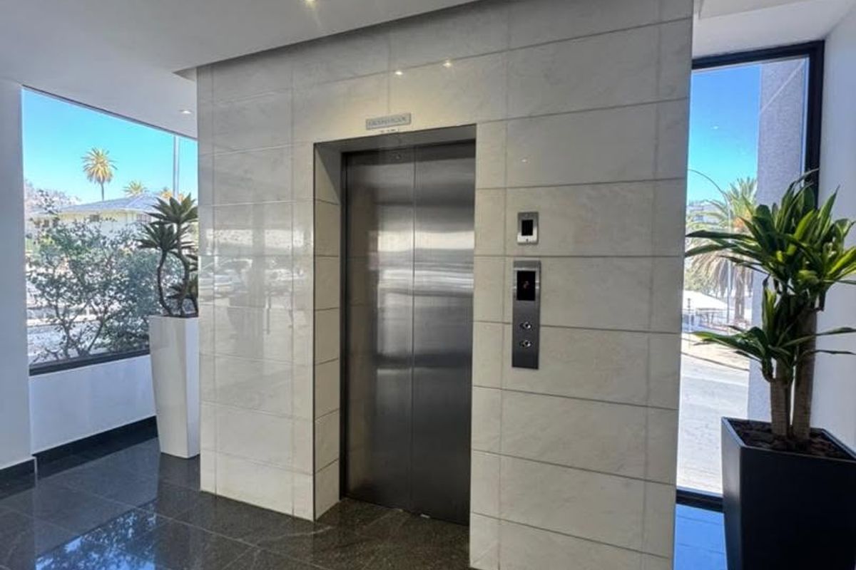 Modern office building lobby featuring a stainless steel elevator, polished stone floor tiles, and elegant stone wall cladding with recessed lighting.