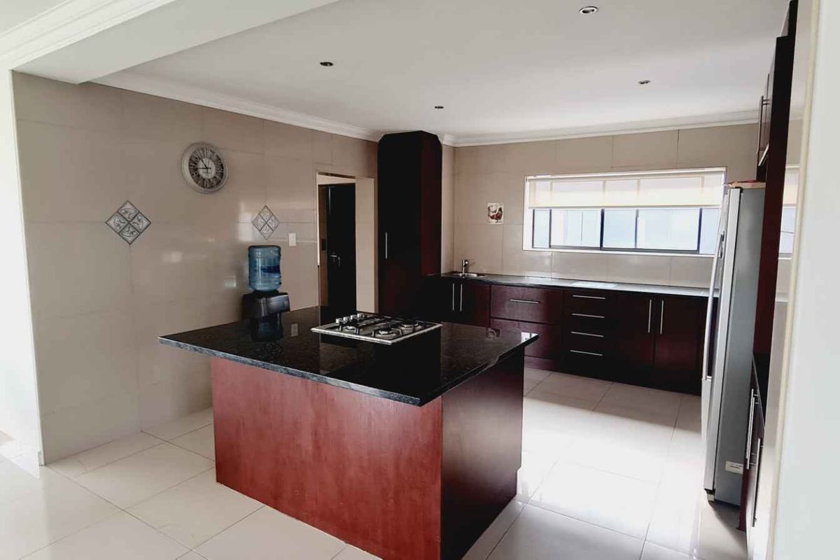 Modern kitchen featuring a central island with a granite countertop, dark wood cabinetry, gas hob, and neutral tiled flooring.