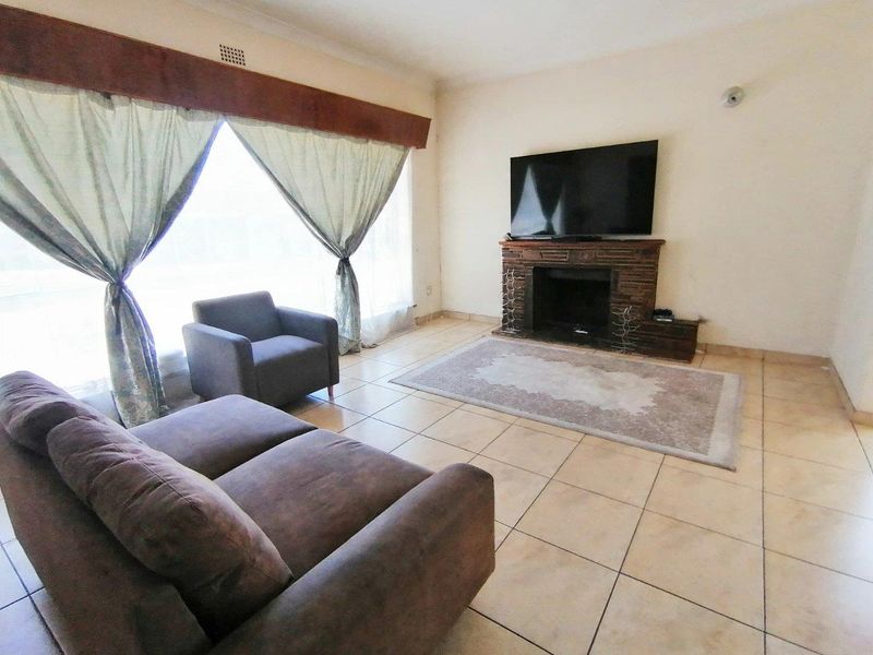 A living room featuring tiled flooring and a brick-faced fireplace, offering a functional space with natural light from the large window.
