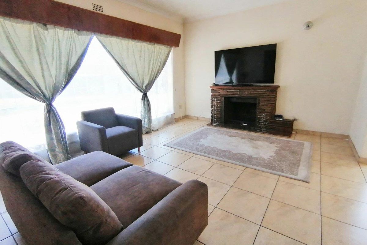 A living room featuring tiled flooring and a brick-faced fireplace, offering a functional space with natural light from the large window.