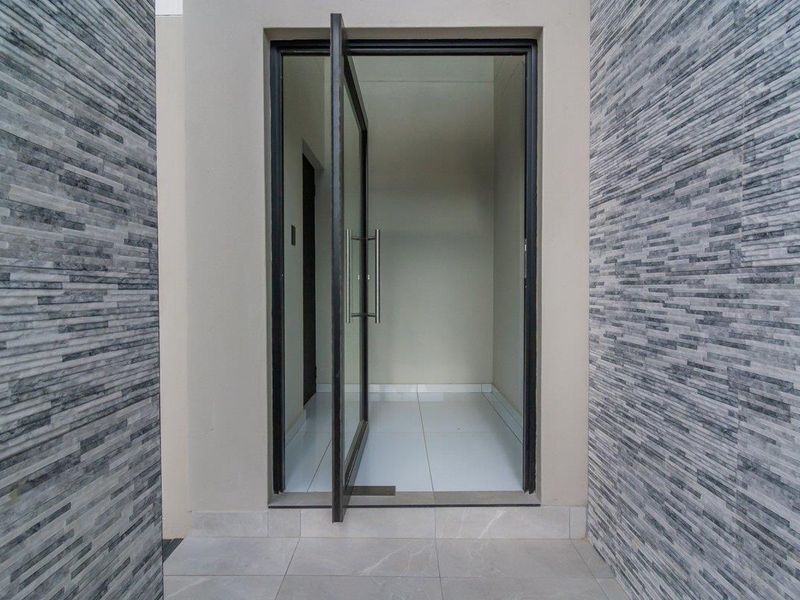 Modern entrance featuring a sleek pivot door, contemporary stacked stone wall cladding, and clean porcelain floor tiles.