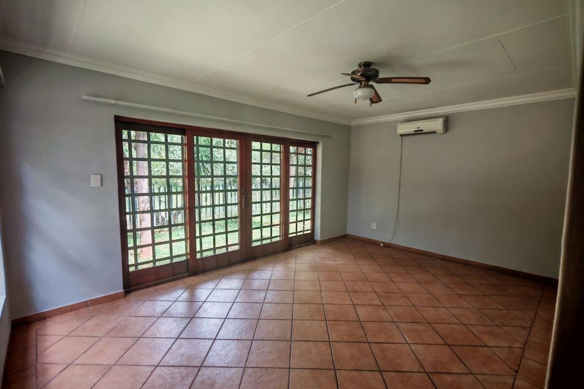 Spacious living area featuring terracotta floor tiles, a ceiling fan, and large wooden-framed sliding doors providing direct access to the garden.