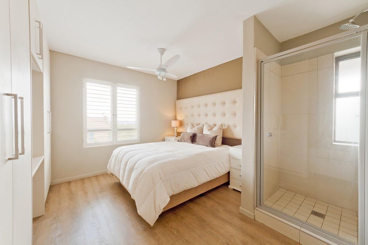 A modern bedroom featuring light wood-look flooring, built-in cabinetry, and an integrated en-suite shower with glass enclosure.