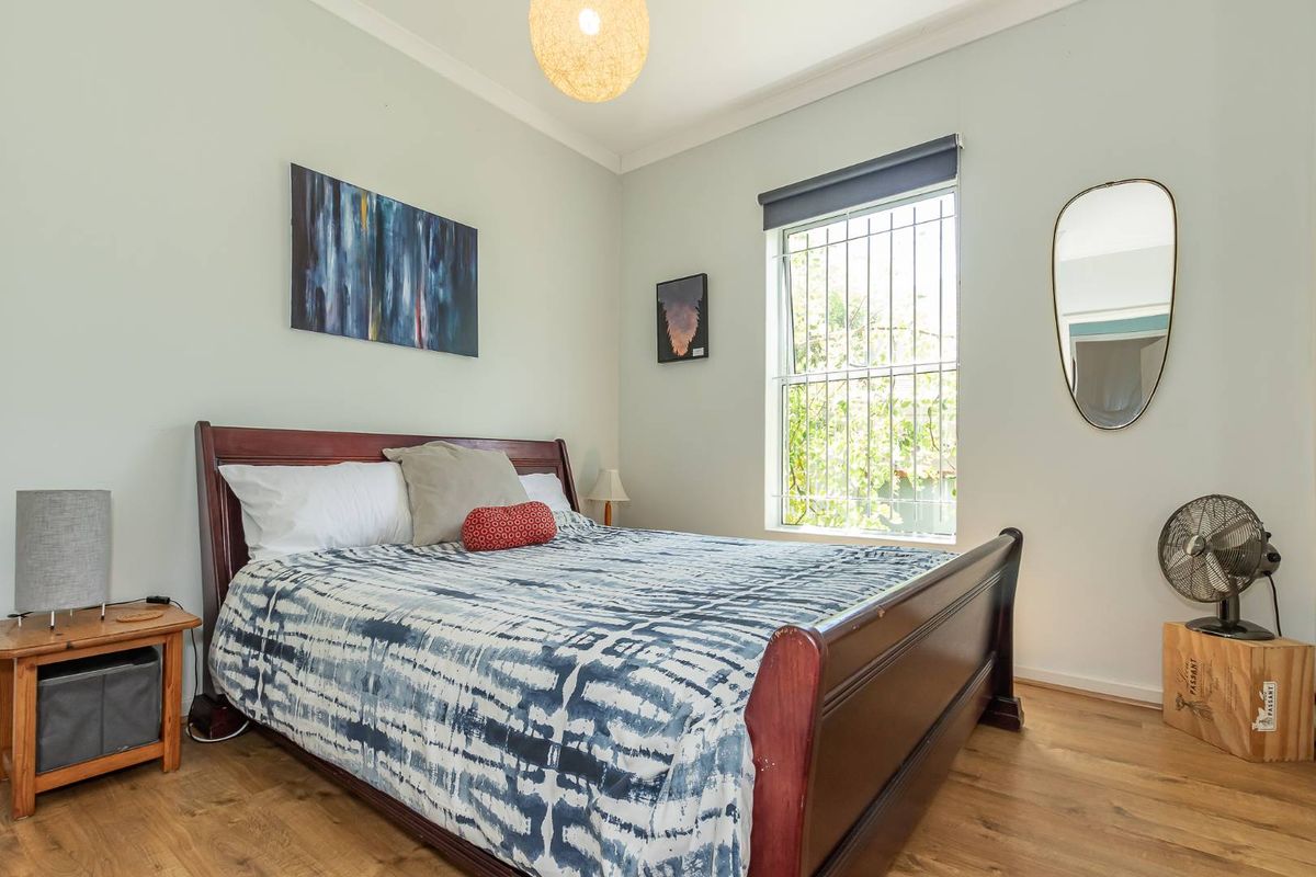 A well-lit bedroom featuring laminate wood flooring, a window with security bars, and neutral wall finishes.