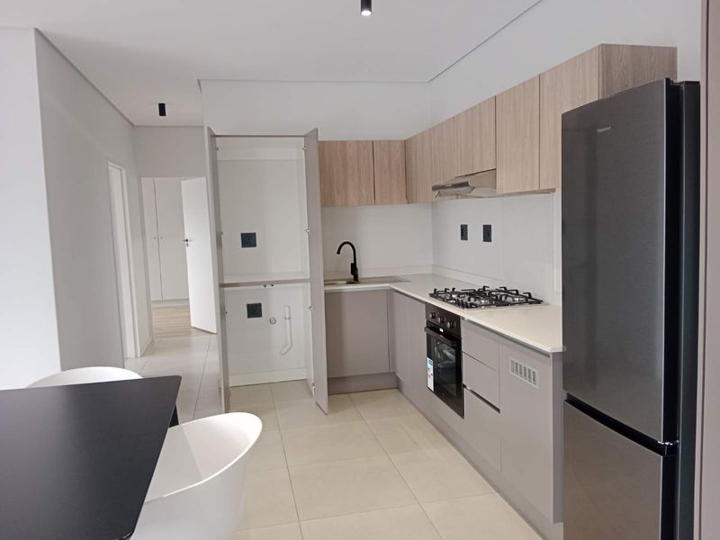 Modern kitchen featuring light wood and grey cabinetry, stone countertops, gas hob, built-in oven, and a dedicated integrated laundry cupboard.