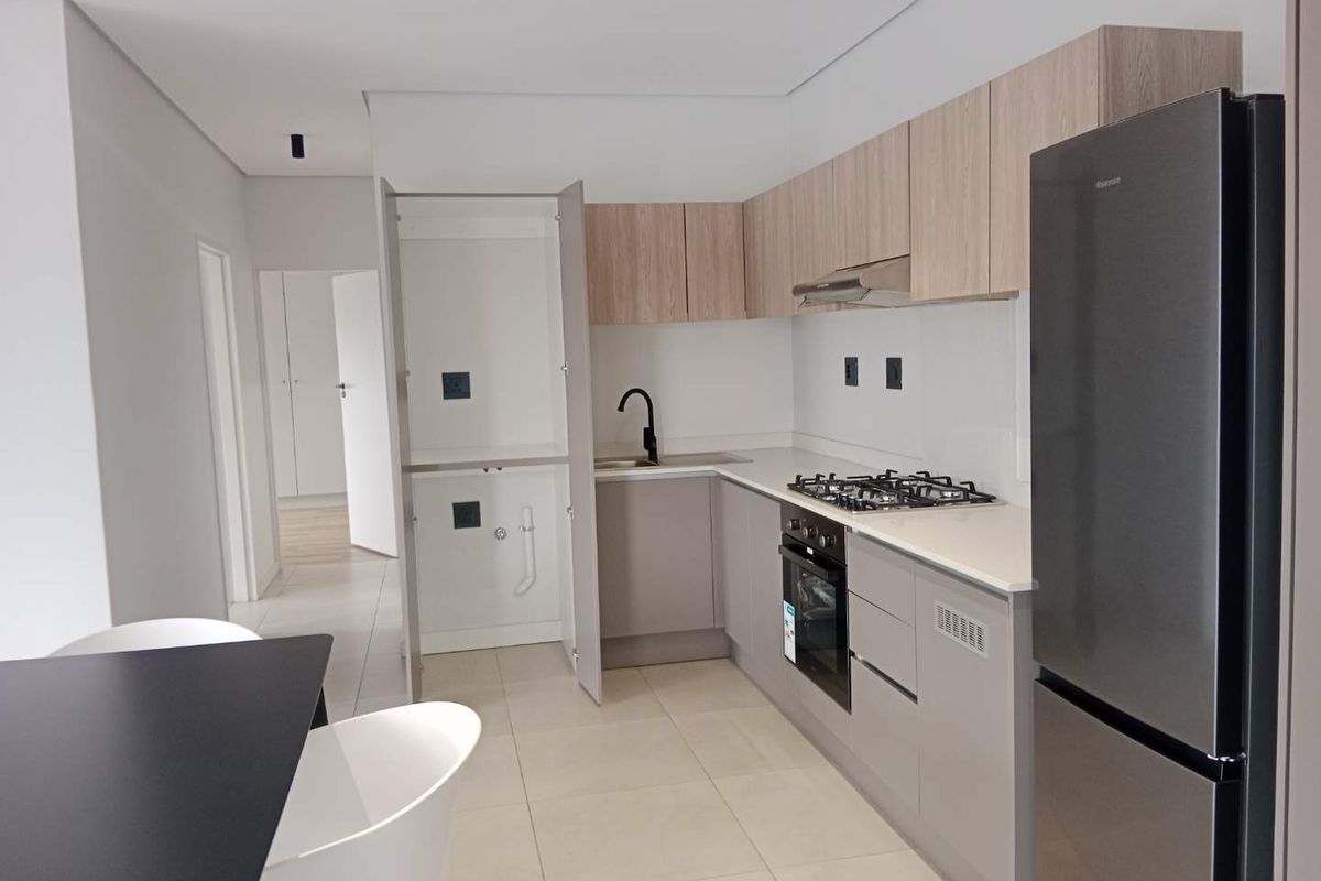 Modern kitchen featuring light wood and grey cabinetry, stone countertops, gas hob, built-in oven, and a dedicated integrated laundry cupboard.