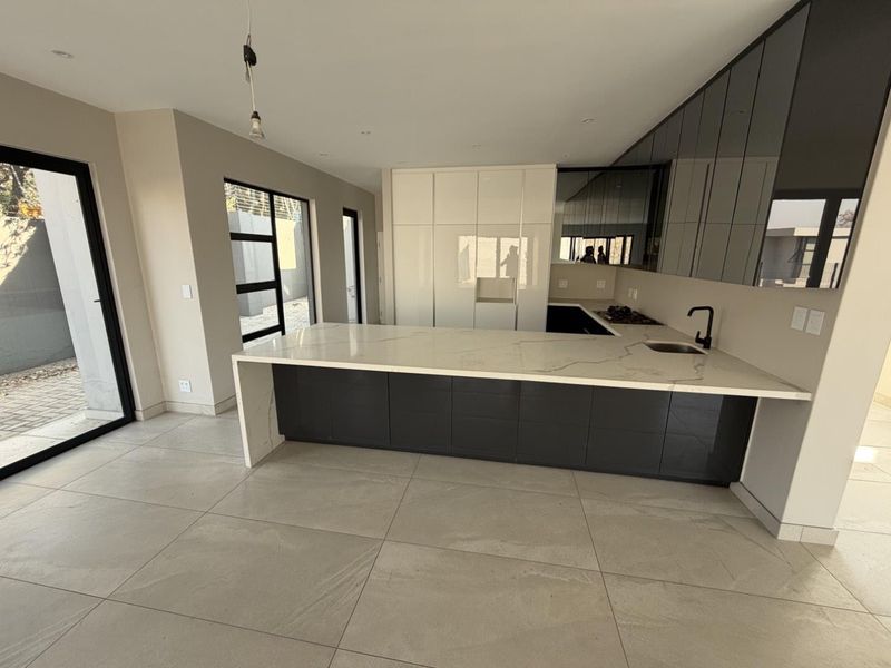 Modern kitchen featuring a large stone waterfall island, sleek dark cabinetry, integrated cooktop, and large glass sliding doors leading to the exterior.