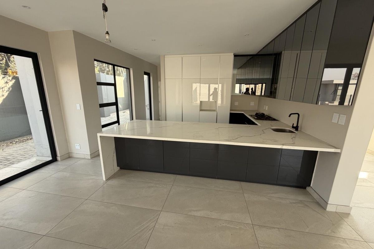 Modern kitchen featuring a large stone waterfall island, sleek dark cabinetry, integrated cooktop, and large glass sliding doors leading to the exterior.