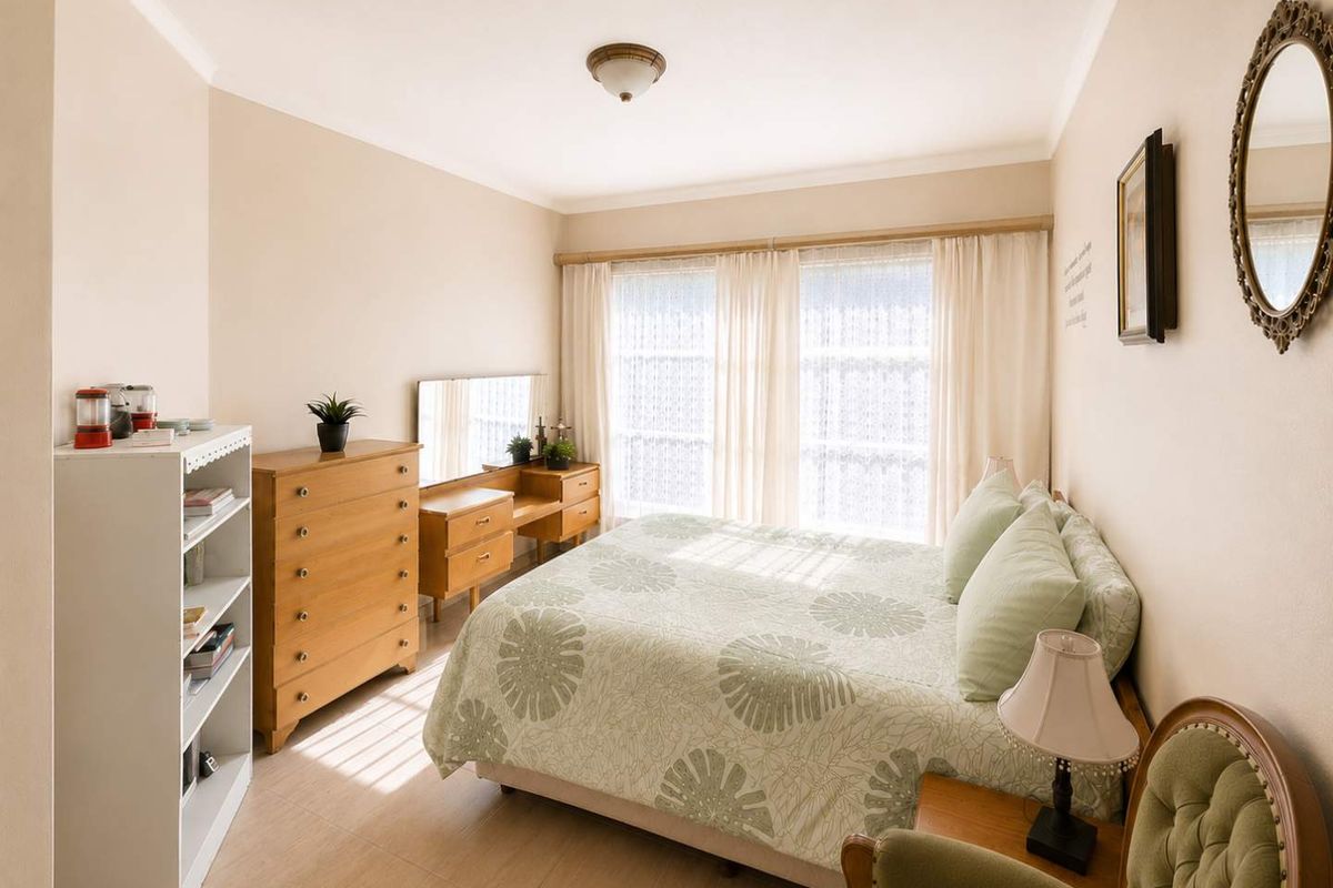A well-lit bedroom featuring neutral wall tones, tiled flooring, and large windows with curtain rails, offering a comfortable and functional living space.