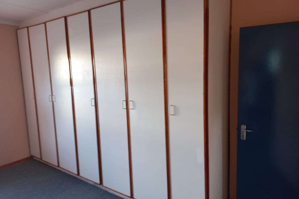 A bedroom featuring extensive floor-to-ceiling built-in cupboards with white doors and timber trim.