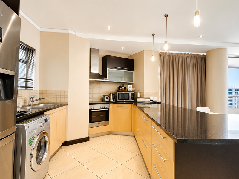 Modern kitchen featuring light wood cabinetry, granite countertops, stainless steel appliances, and a breakfast bar, seamlessly integrated into an open-plan living space.