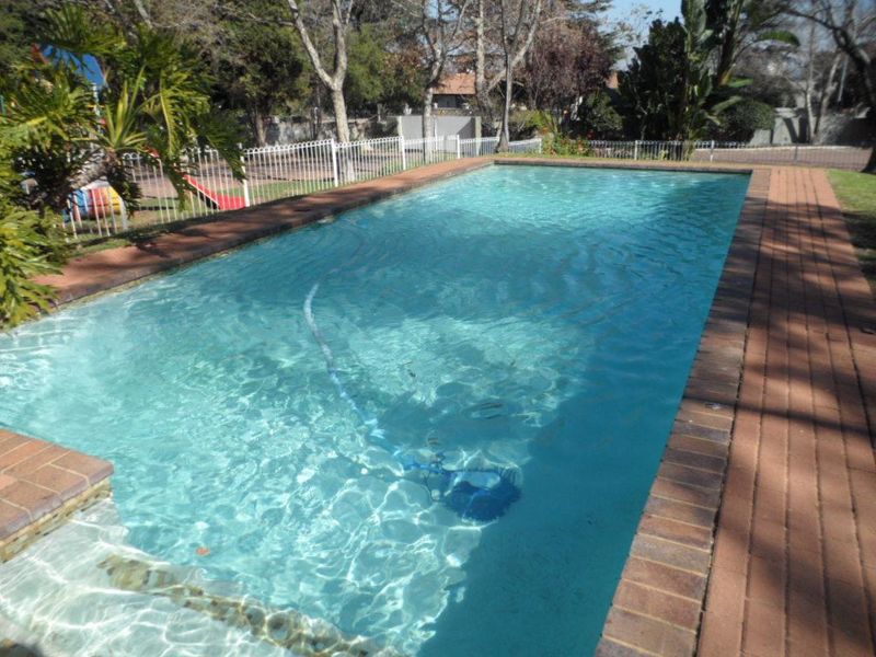 A rectangular swimming pool featuring brick coping and secure metal perimeter fencing, set within a landscaped outdoor area.