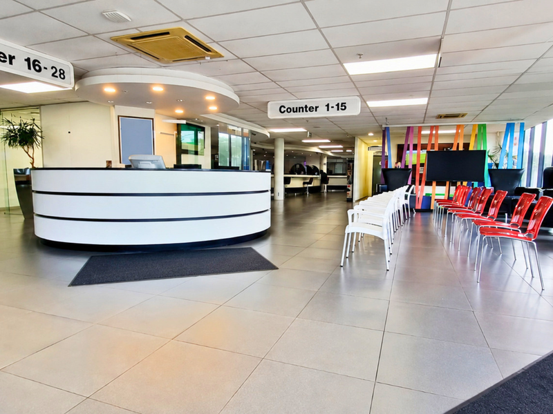 A spacious, modern office reception area featuring a curved service desk, tiled flooring, and suspended ceiling with integrated lighting.