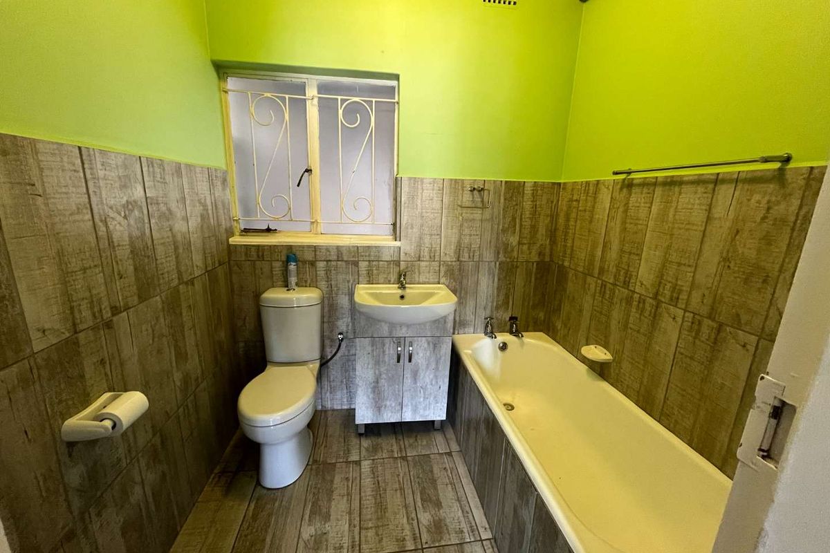A functional bathroom featuring a bathtub, vanity basin with storage cabinet, and toilet, finished with wood-look wall and floor tiling.