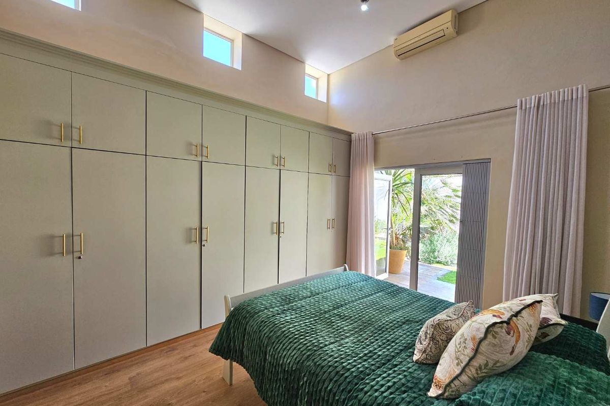 Spacious bedroom featuring extensive floor-to-ceiling built-in cabinetry, high ceilings with clerestory windows, and direct access to the garden through sliding glass doors.