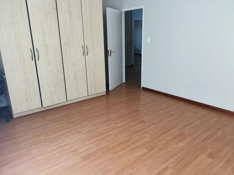 A clean, empty bedroom featuring light wood-tone built-in cupboards and warm laminate flooring, offering a neutral canvas for personalization.