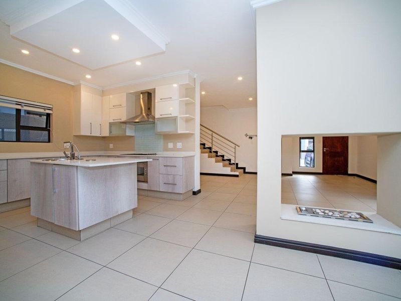 Spacious open-plan kitchen and living area featuring a modern kitchen island, built-in appliances, recessed lighting, and a central fireplace, leading to a staircase.