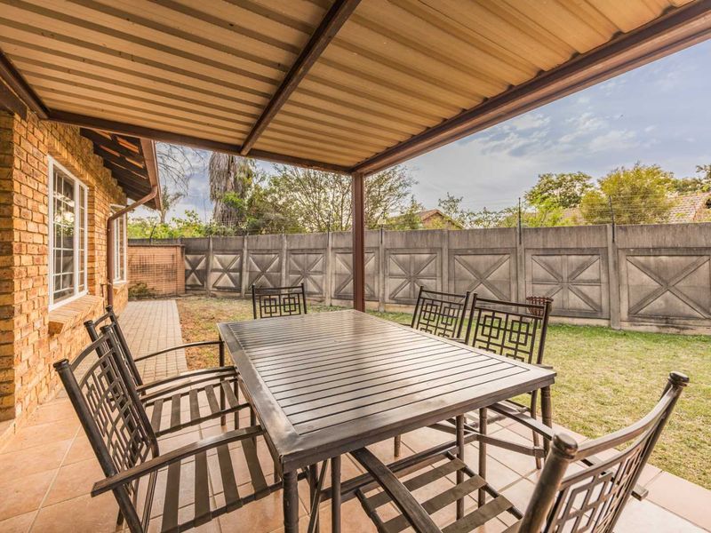 A covered patio area featuring tiled flooring and a corrugated metal roof, overlooking a private garden enclosed by precast concrete boundary walls.