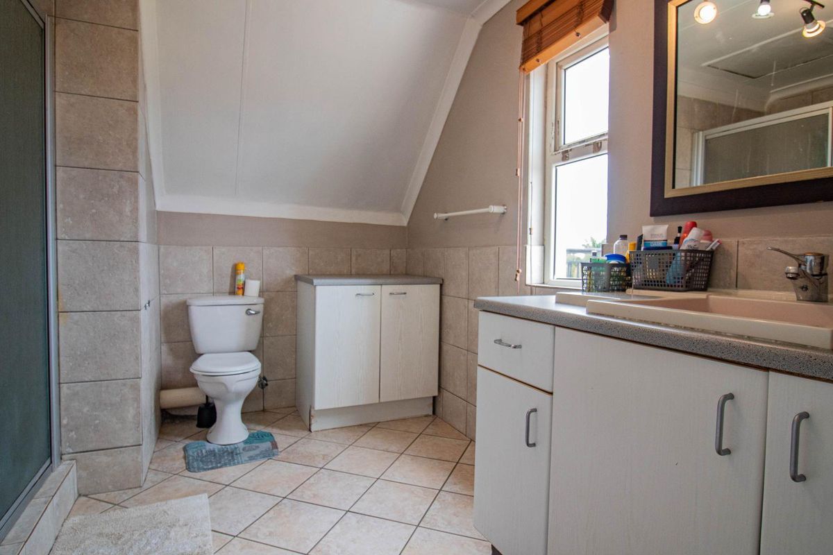 A functional bathroom featuring a shower enclosure, a built-in vanity with a basin, and a toilet, set under a sloped ceiling with natural light.